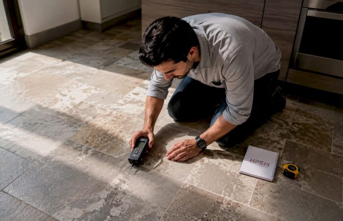 Hands using moisture meter on flooring surface